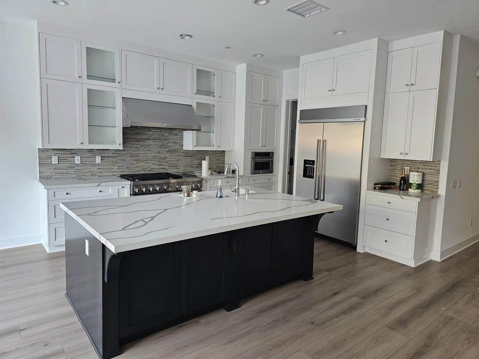 Kitchen before removal with white shaker cabinets, glass-front uppers, a dark island and a white quartz countertop
