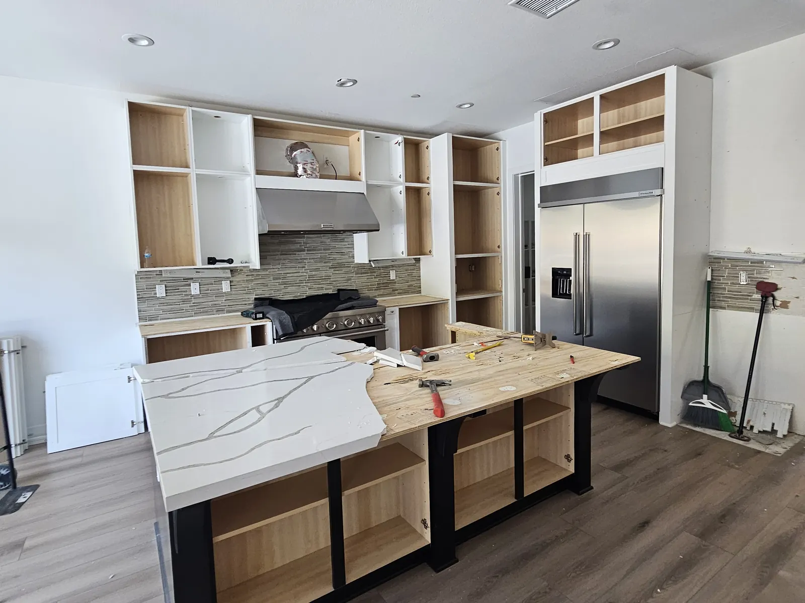 The same kitchen mid-removal: cabinet doors off, open cabinet boxes, and the island countertop partly taken apart